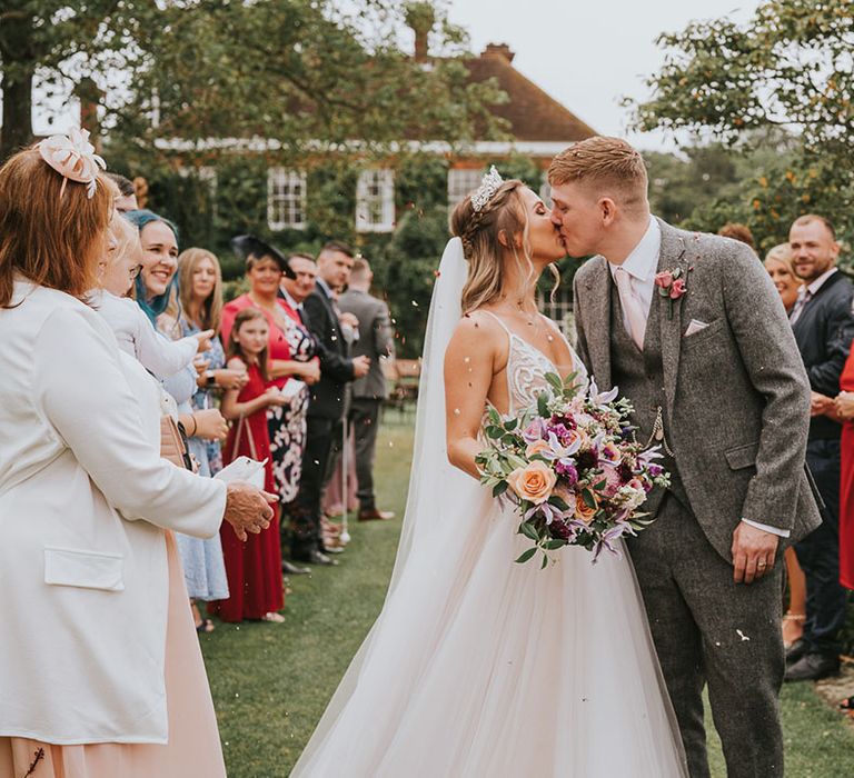 Bride and groom share a kiss in front of their wedding guests outside of wedding venue at country house