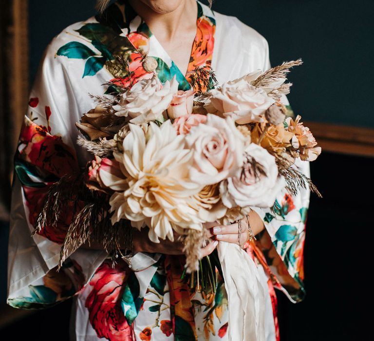 Bride in silk floral dressing gown and neutral autumn themed wedding bouquet