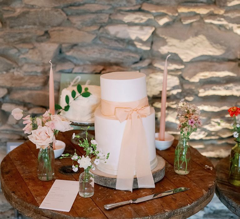 Two tier white wedding cake with pink bow on a table with pink candles and roses 