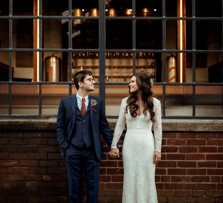 Bride and groom hold hands and look at each other with bride in Maggie Sottero dress with flower hair accessory 