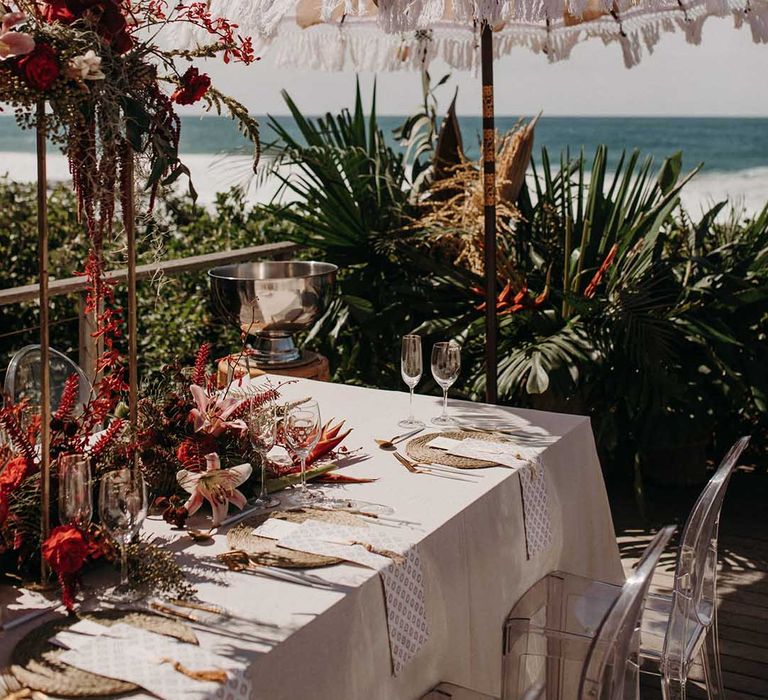 Tropical beach wedding setting for destination wedding in South Africa with white umbrella with tassel trim, red and pink flowers