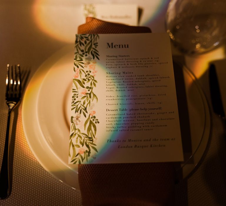 Wedding menu card with leaf detail and pink flowers on orange napkin