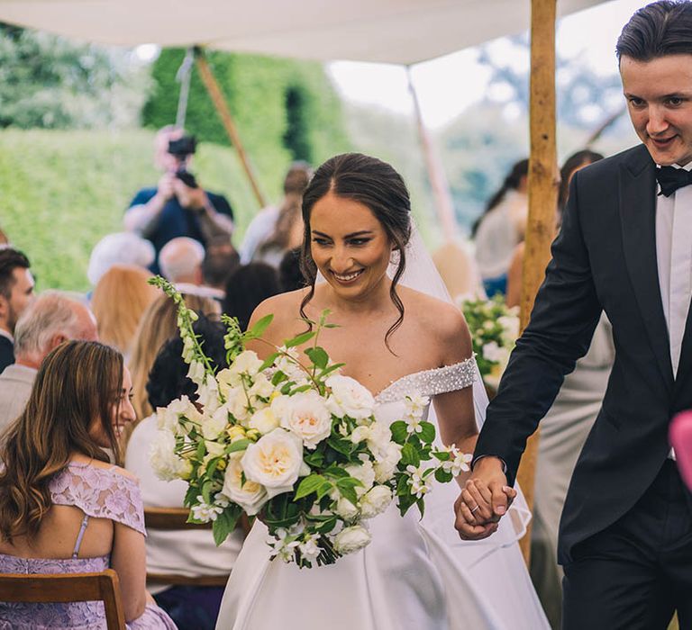 Bride and groom walk back down the aisle as a married couple with all white wedding bouquet 