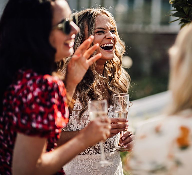 Bride laughs and socialises with wedding guests holding glass of champagne 