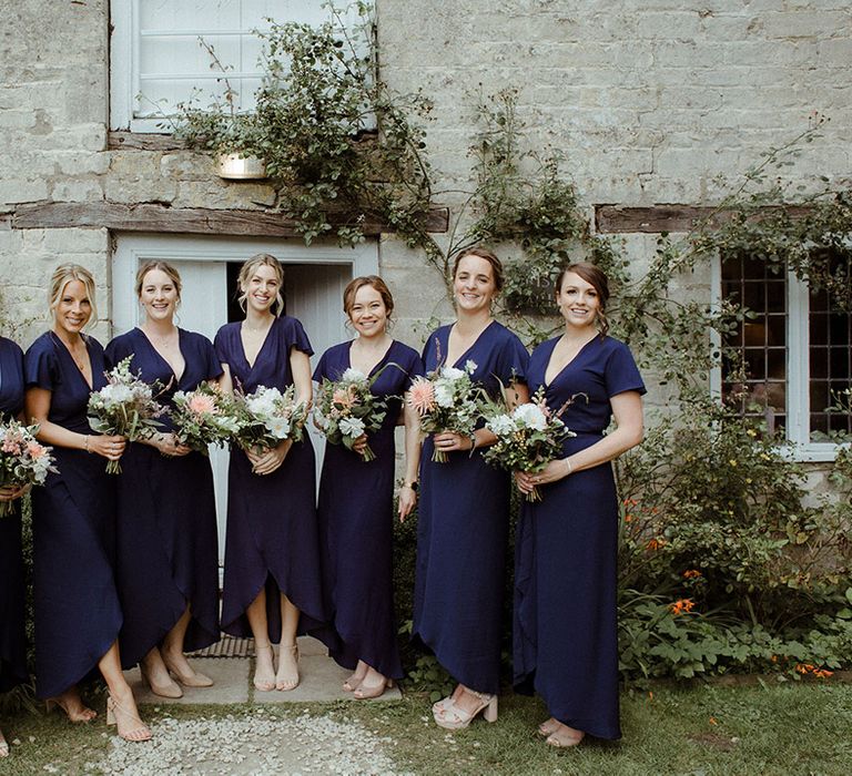 Seven bridesmaids in navy blue dresses with butterfly sleeves and nude wedding shoes holding white and pink bouquets 