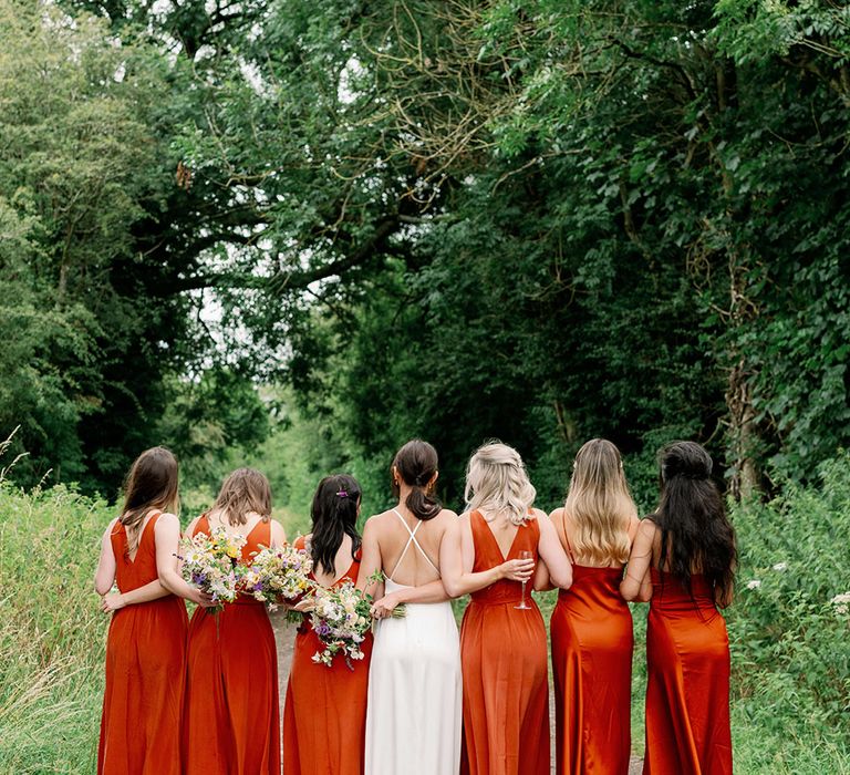 Bride stands with her bridesmaids who wear orange silk slip dresses from & Other Stories 