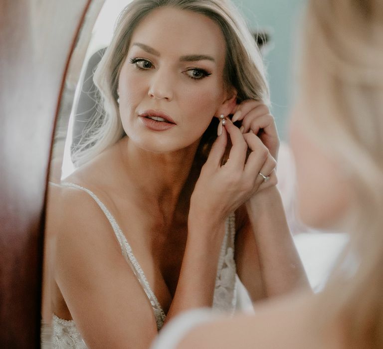 Bride with curled blonde hair puts in pearl earrings 