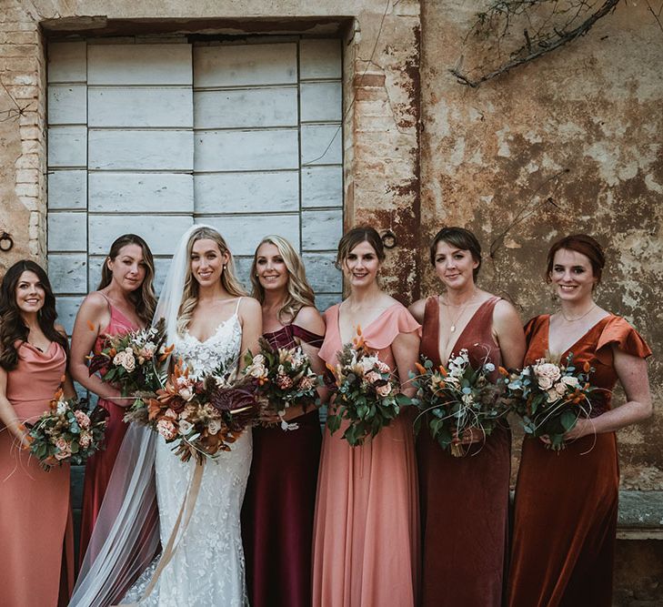 Bridesmaids wear different styled dresses in shades of orange and red 