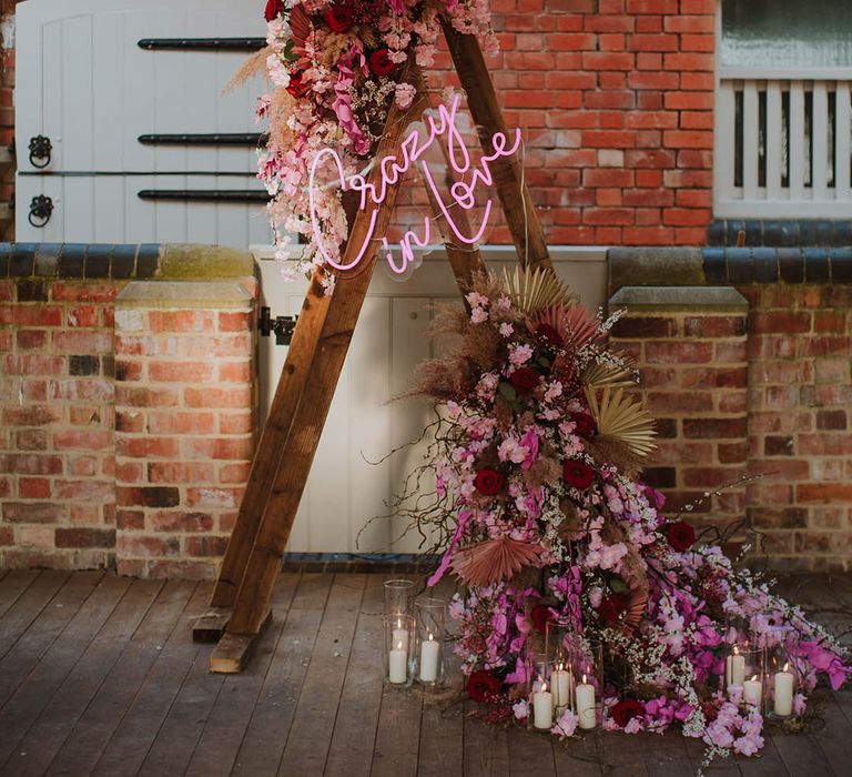 Pink flowers surround a pink neon 'Crazy In Love' wedding sign 