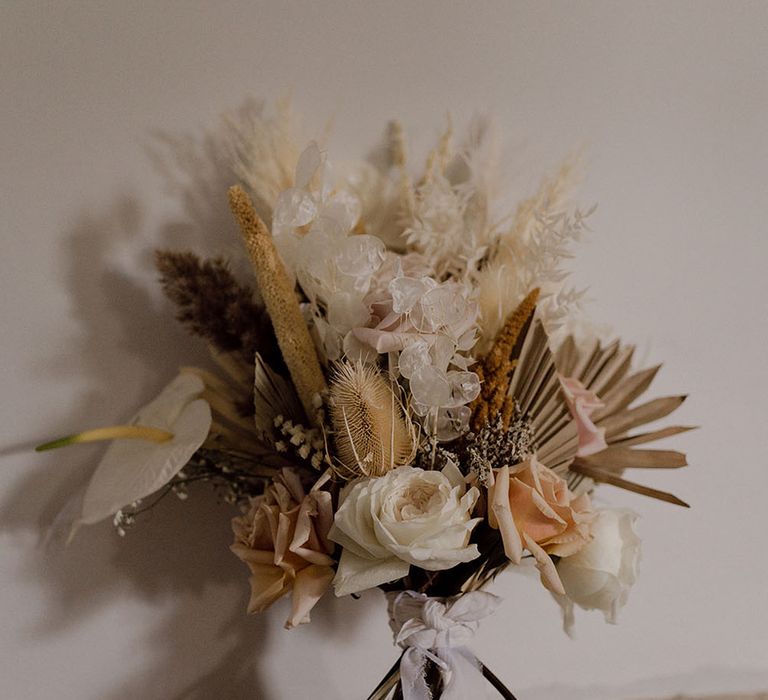 Dried flower bouquet featuring white anthurium, pastel roses and pampas grass tied with white ribbon