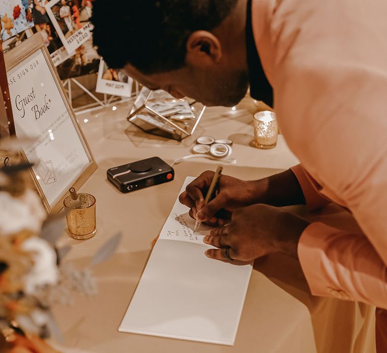 Wedding guest signs guest book on table surrounded by personal photos 