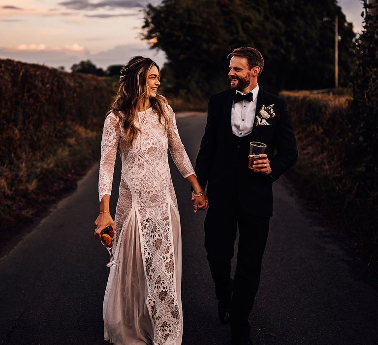 Groom in black tie holds a pint of beer with the bride in a boho lace wedding dress holding an Aperol Spritz 