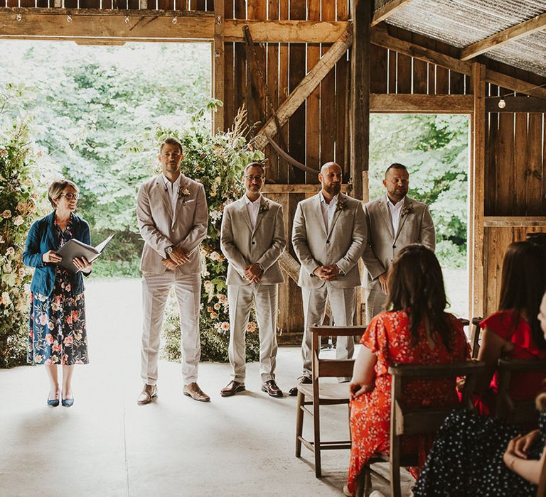 Groomsmen in light wedding suits standing next to the groom as he waits patiently for the bride 