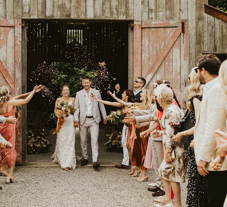 Bride and groom walk out of the Nancarrow Farm wedding venue in Cornwall as wedding guests throw confetti 