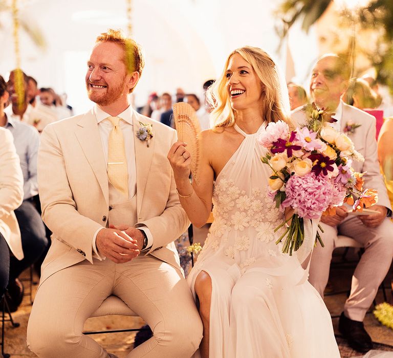 Bride and groom sit for their wedding ceremony with a fan in the hot Italian summer weather 