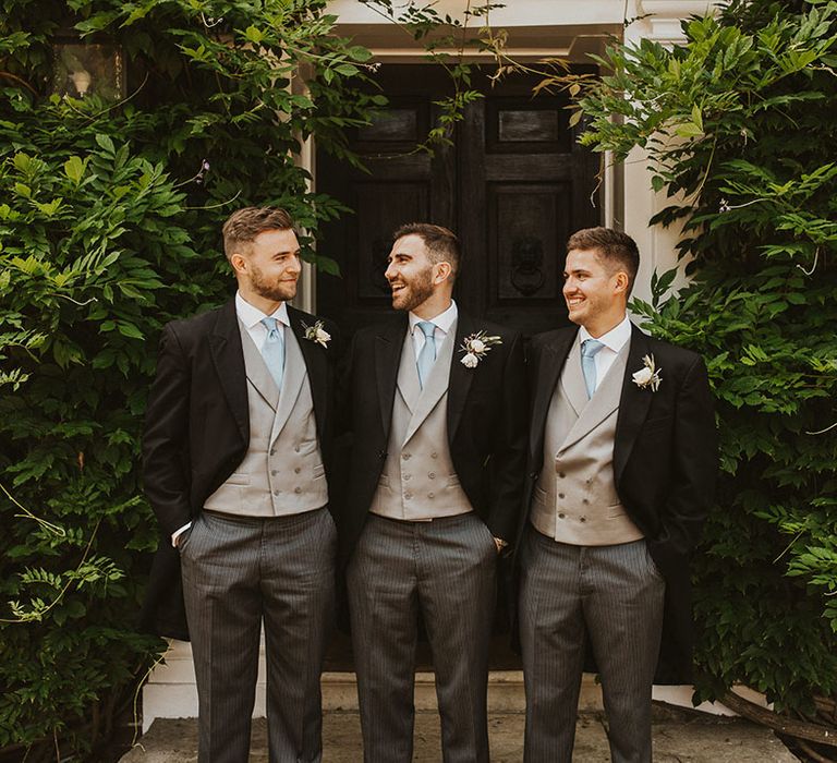 Groom with two of his groomsmen in a morning suit, light grey waistcoat, and pale blue tie 