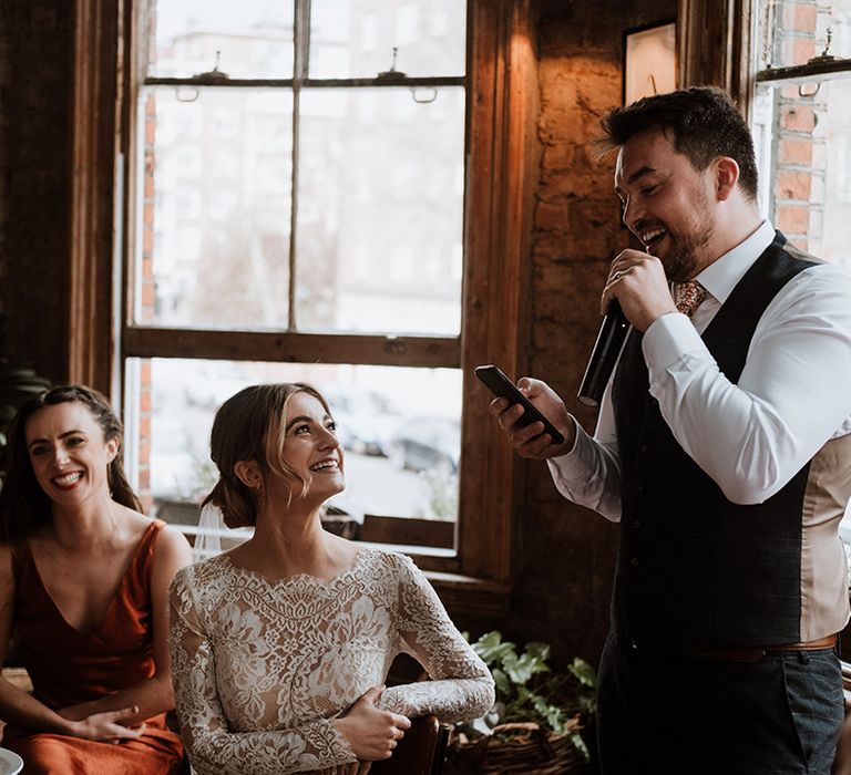 Bride in lace wedding dress listens to speeches during pub reception 