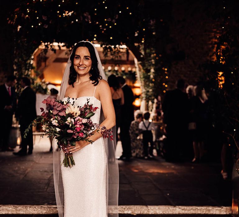 Bride in a beaded sparkle wedding dress with train holding a dark pink bouquet of flowers for barn wedding 