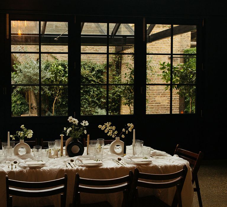 Minimalistic wedding tablescape at 100 Barrington wedding venue with black and white circular vases and white floral arrangements, white tablecloth, and gold cutlery