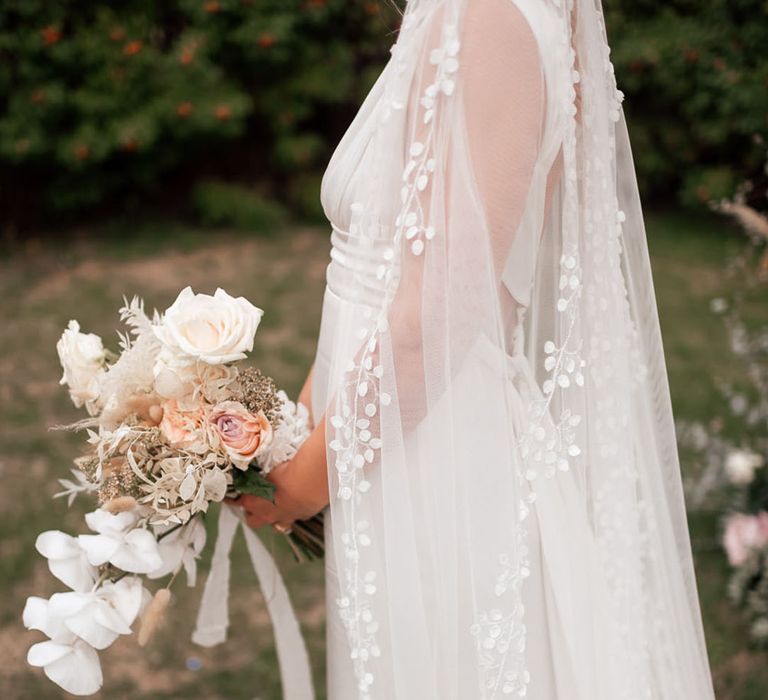 Close up of the bride's wedding veil with leaf and floral design holding a neutral bouquet