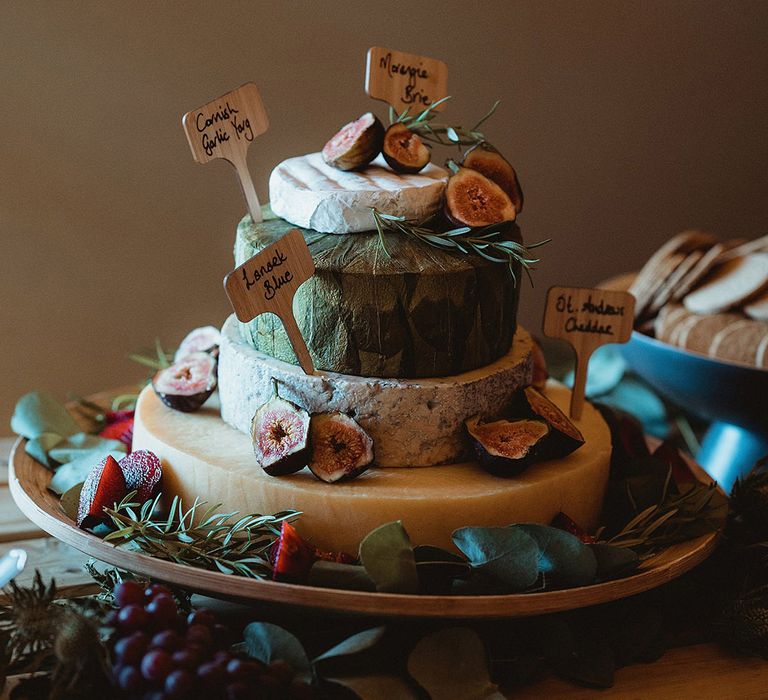 Signposted wedding cheese tower with grapes and greenery on a table with crackers and chutney for wedding guests 