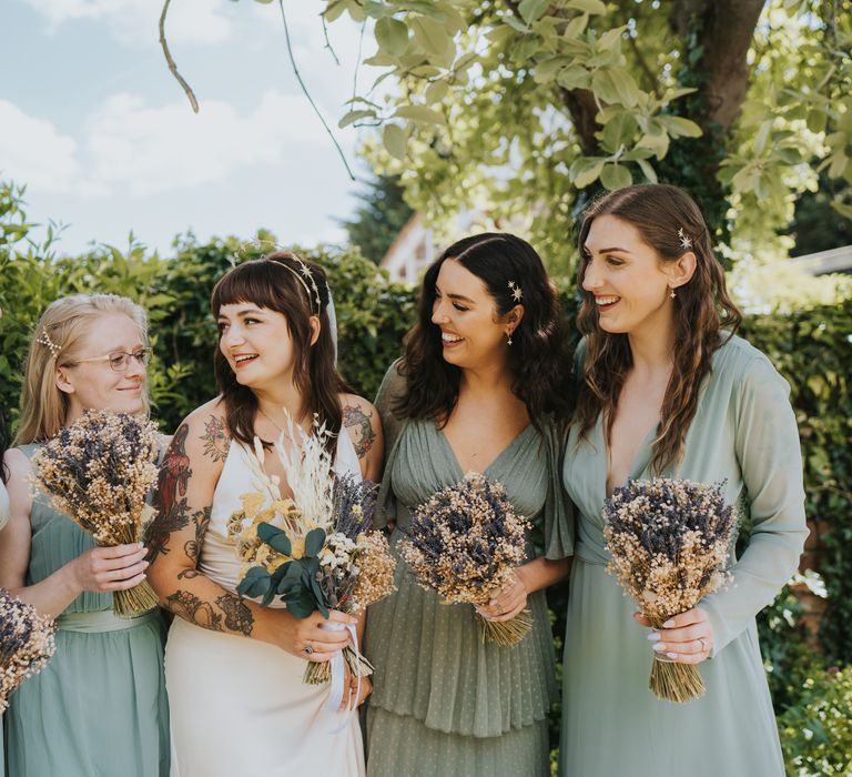 Bride in v-neck ASOS silk wedding dress with gold halo wedding headpiece with bridesmaids in mismatched sage green bridesmaid dresses 