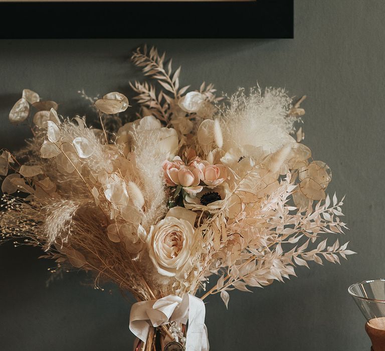 Bride's white bouquet with roses, poppies, and dried grass tied up with white ribbon 