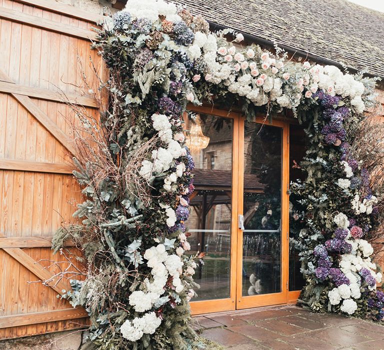 White, pink, and purple wedding flower arch with twigs made up of roses and hydrangeas decorating Notley Abbey