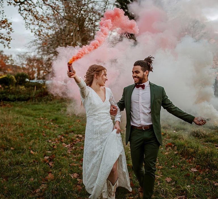 Bride in  long sleeve lace wedding dress and groom in classic black suit with burgundy bowtie doing hot pink smoke bomb photo shoot 