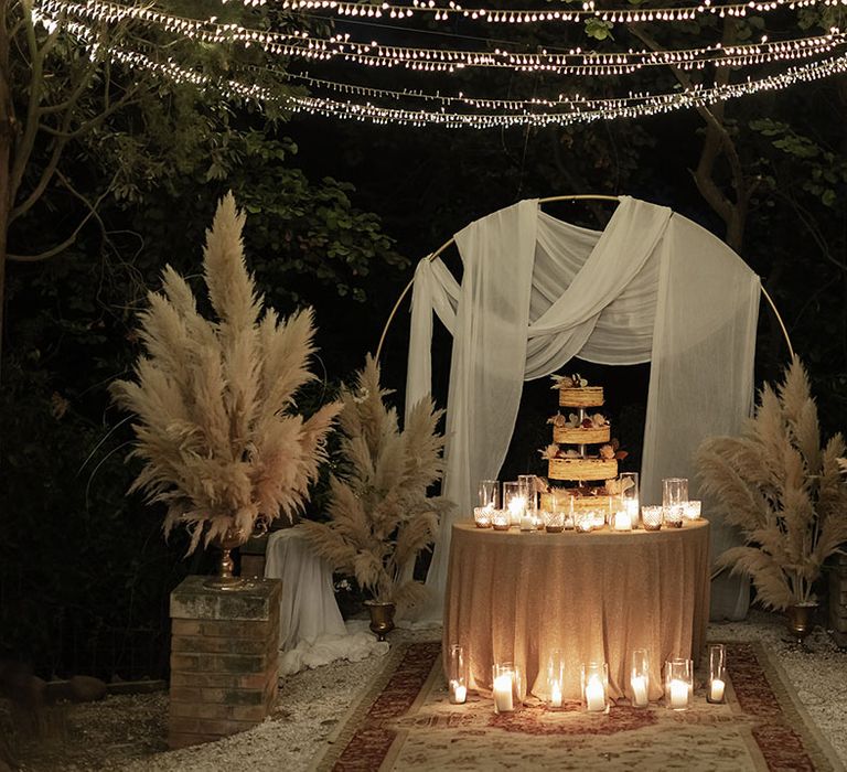 Four tier Opera cake sits on round table beside white pillar candles and drapes 