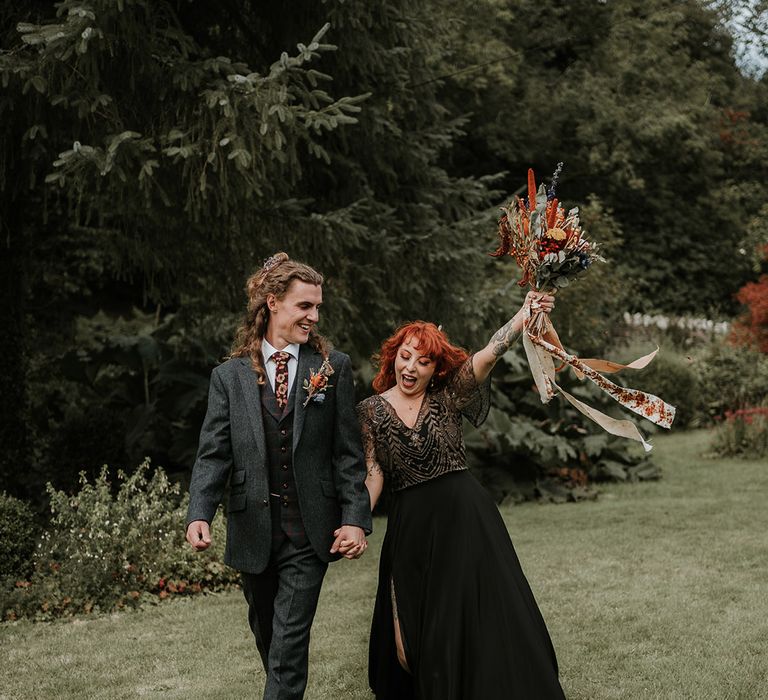 Groom in dark grey three piece suit and burgundy flower patterned tie and bride in black dress for wedding in Devon 