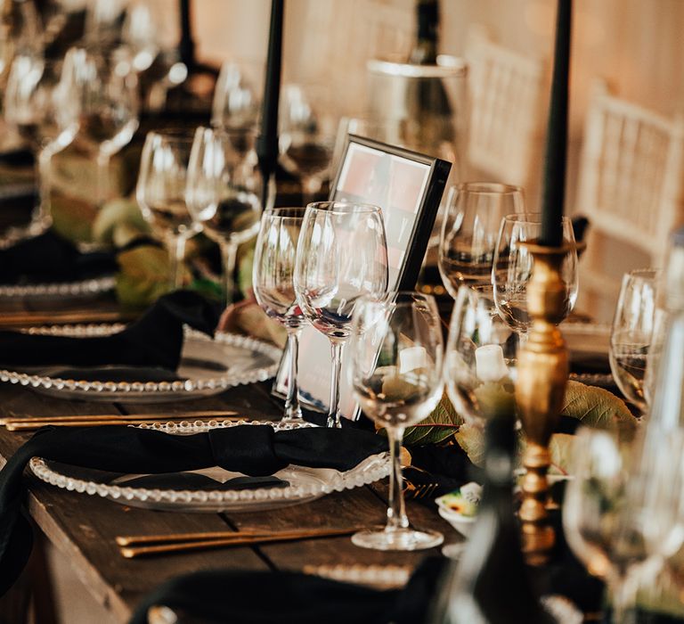 Beaded charger plates with black napkins, black place names, and black taper candles, gold cutlery, gold rimmed glasses, and table name sign need after TV show