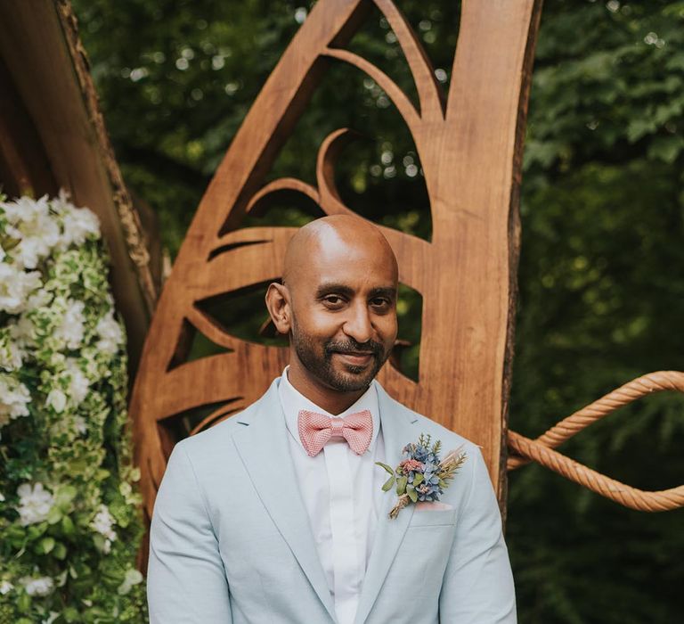 Groom in pastel blue suit with pink bow tie and pink and blue buttonhole accessory 