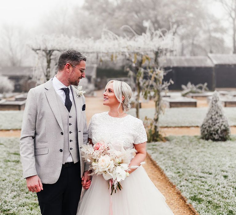 Groom in light grey suit jacket with the bride in a beaded top and skirt bridal separates with a pink and white rose bouquet 