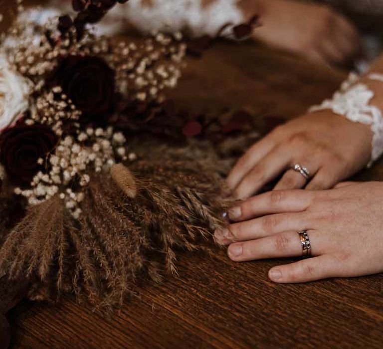 Brides showing off their wedding rings on wooden table with dried flower, pampas grass and baby's-breath flower arragements 