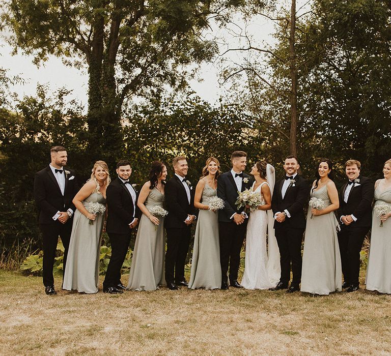 The wedding party with a black tie dress code including tuxedos, green bridesmaid dresses and white bouquets 