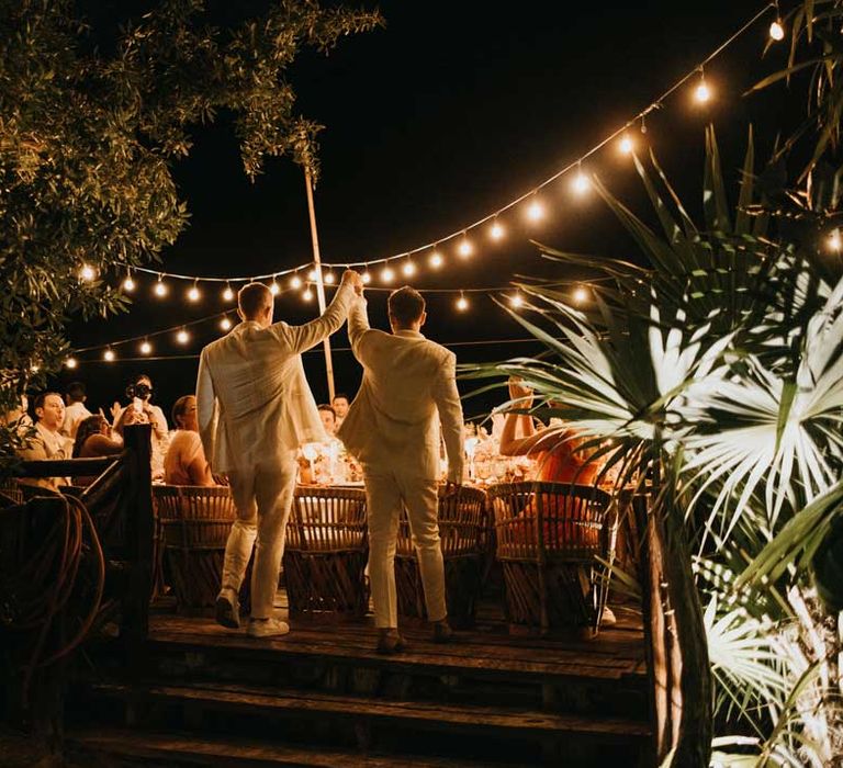 Grooms in complimenting white double breasted grooms suits walking into wedding reception at destination beach wedding in Mexico 