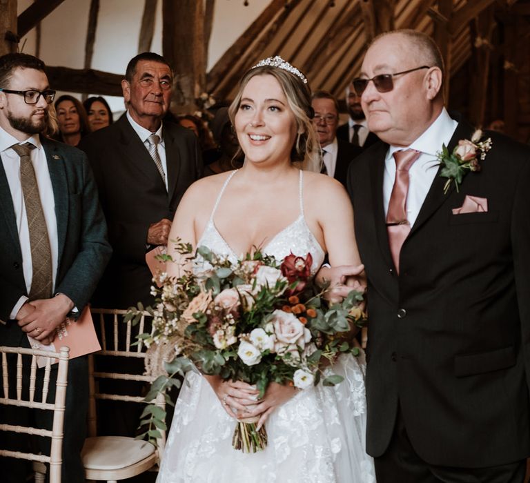 Bride in sparkly beaded wedding dress holding a blush pink and white bouquet with the father of the bride in sunglasses and black and pink suit 