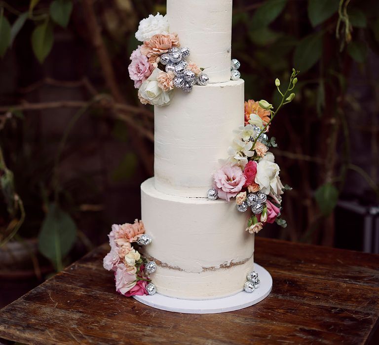 Three tier tall buttercream frosted wedding cake with mini disco ball decorations and pink flowers 