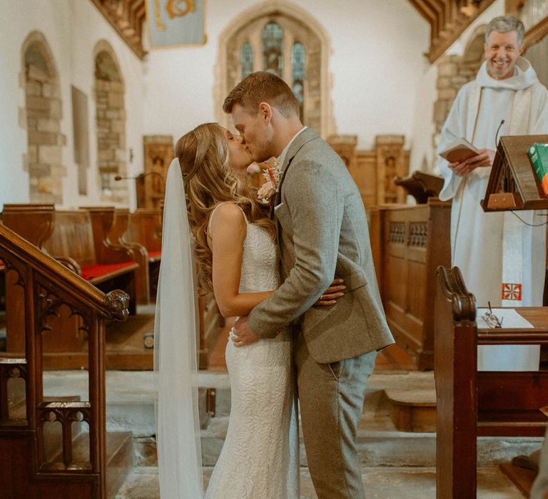 The bride and groom share their first kiss as a married couple at their church wedding in Wales 