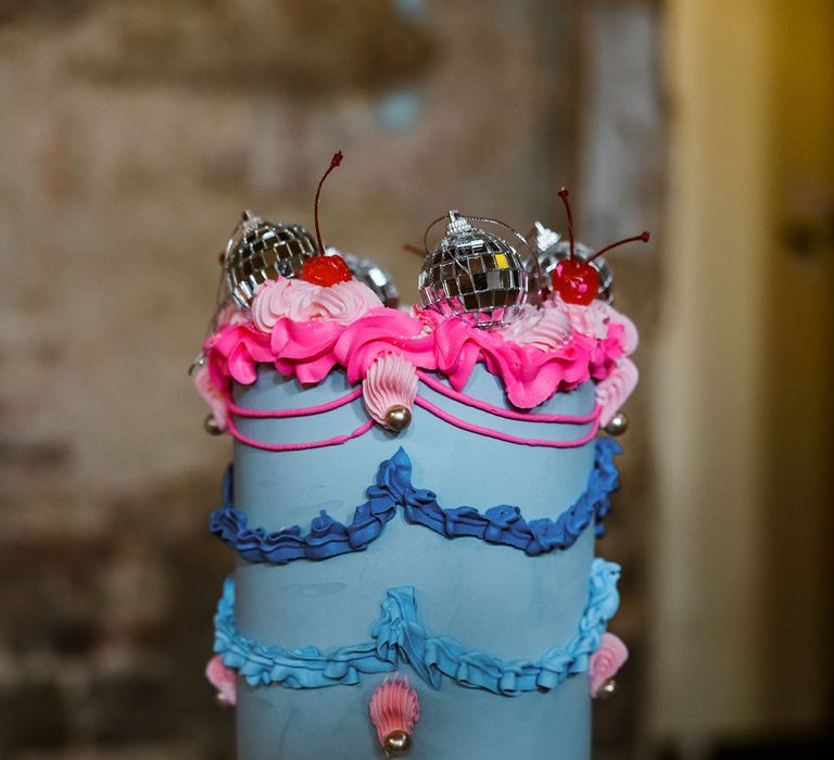 Bright and bold vintage wedding cake with light and dark blue icing with purple and pink piping work with mini disco ball decorations 