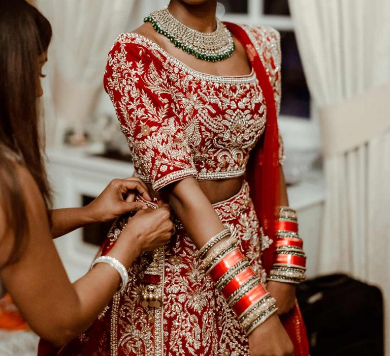 Bridesmaids helping bride into red and gold bridal lehenga 