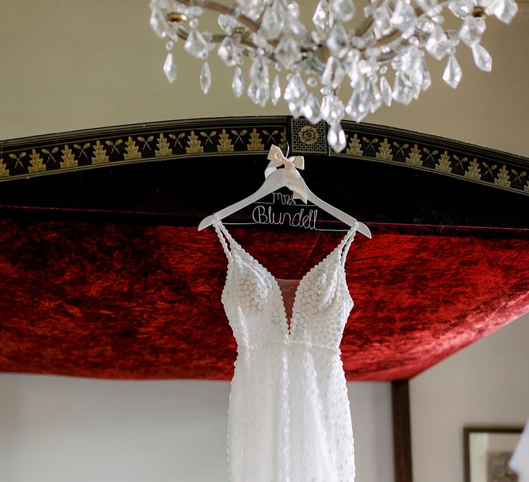 Appliqué Made With Love bridal gown on a personalised wire hanger hanging from a four poster bed 