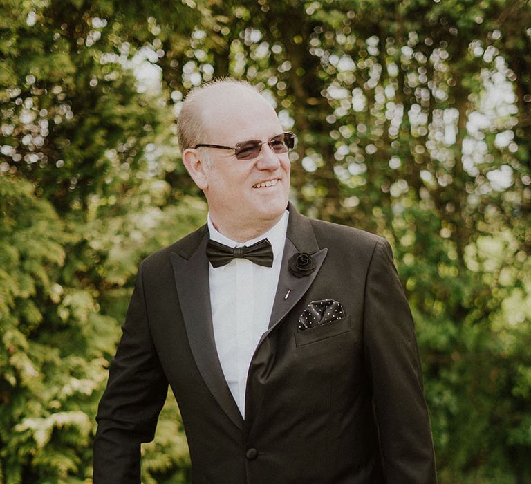 Wedding guest in black tuxedo with black accessories including black pocket square and buttonhole 