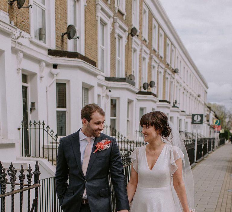 Groom in navy suit with large colourful buttonhole accessory with the bride in a sparkly wedding dress at London city wedding 