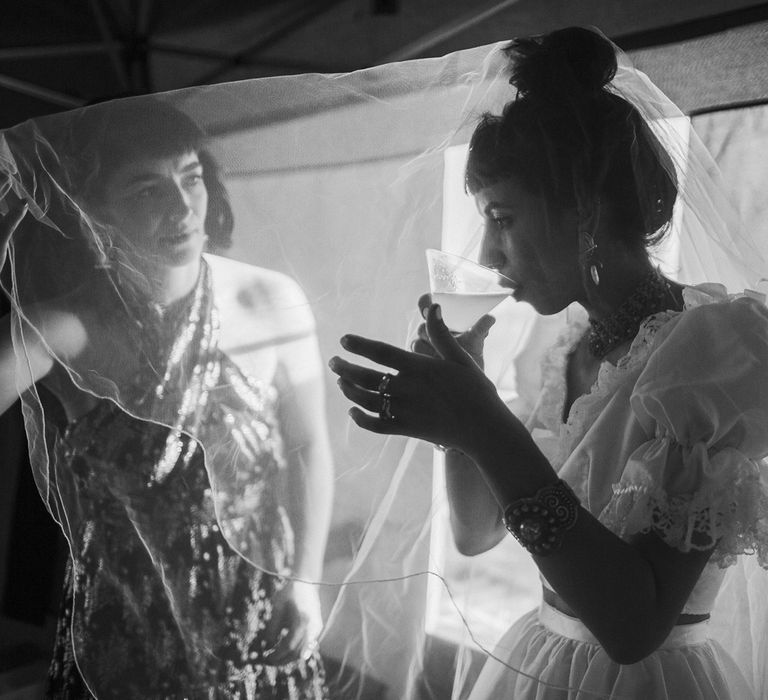 Bride in ruffle bridal separates with wedding updo drinks cocktal under her veil