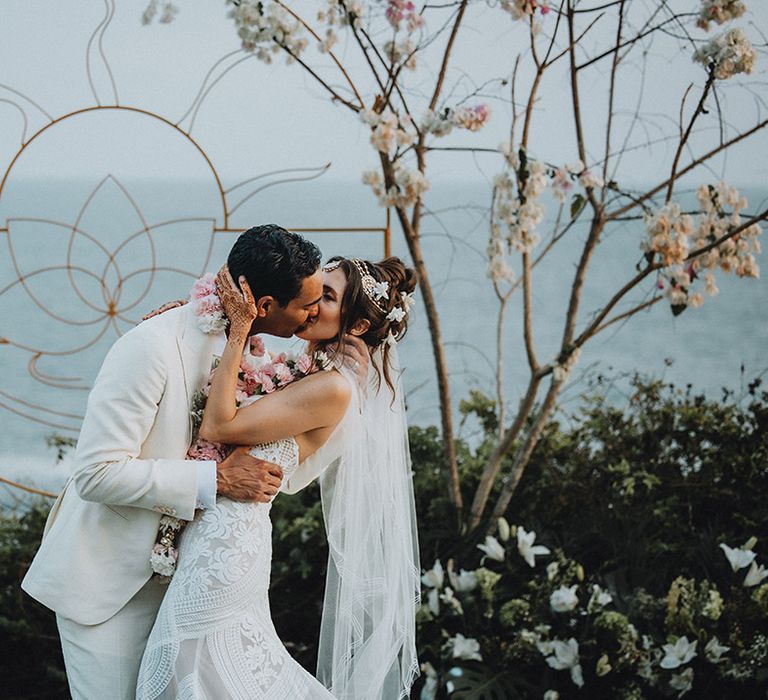 Groom in cream wedding suit kissing boho bride in lace wedding dress at Tigre Del mar wedding ceremony