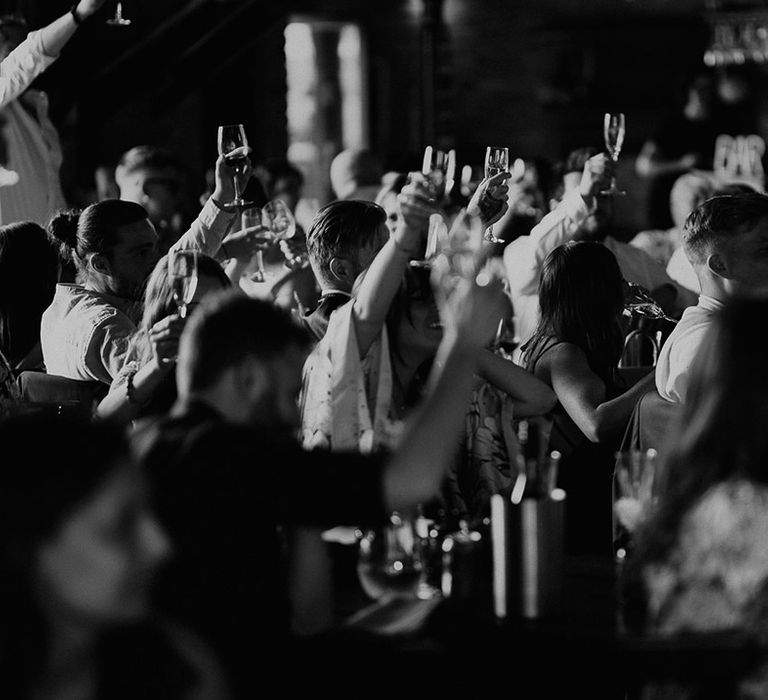 Wedding guests raise their glasses in a toast for the new happy couple 