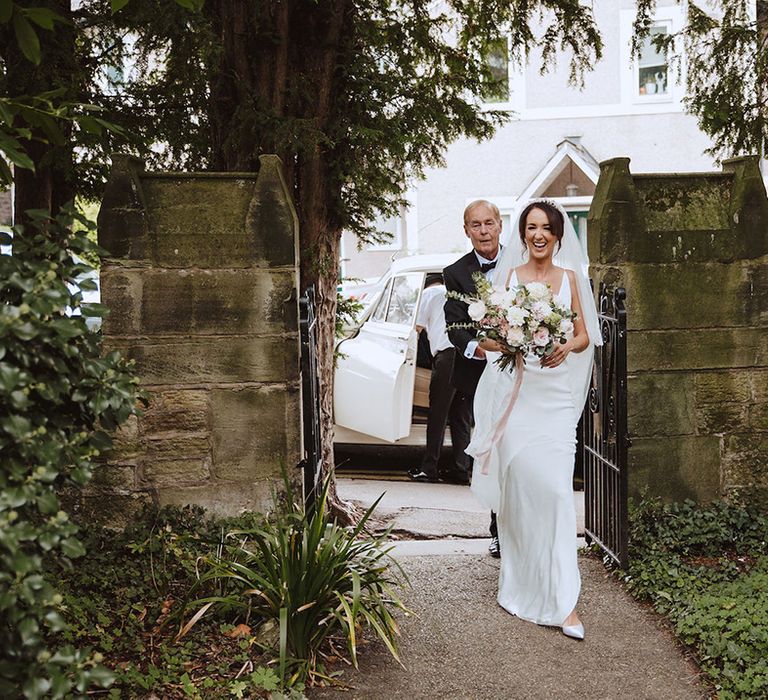 The bride in a satin slip wedding dress walks to the church for a Catholic wedding ceremony 