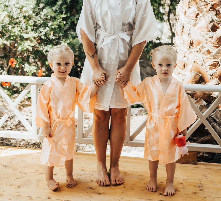 Bride in white bridal robe with flower girls in peach robes for Santorini wedding in Greece 